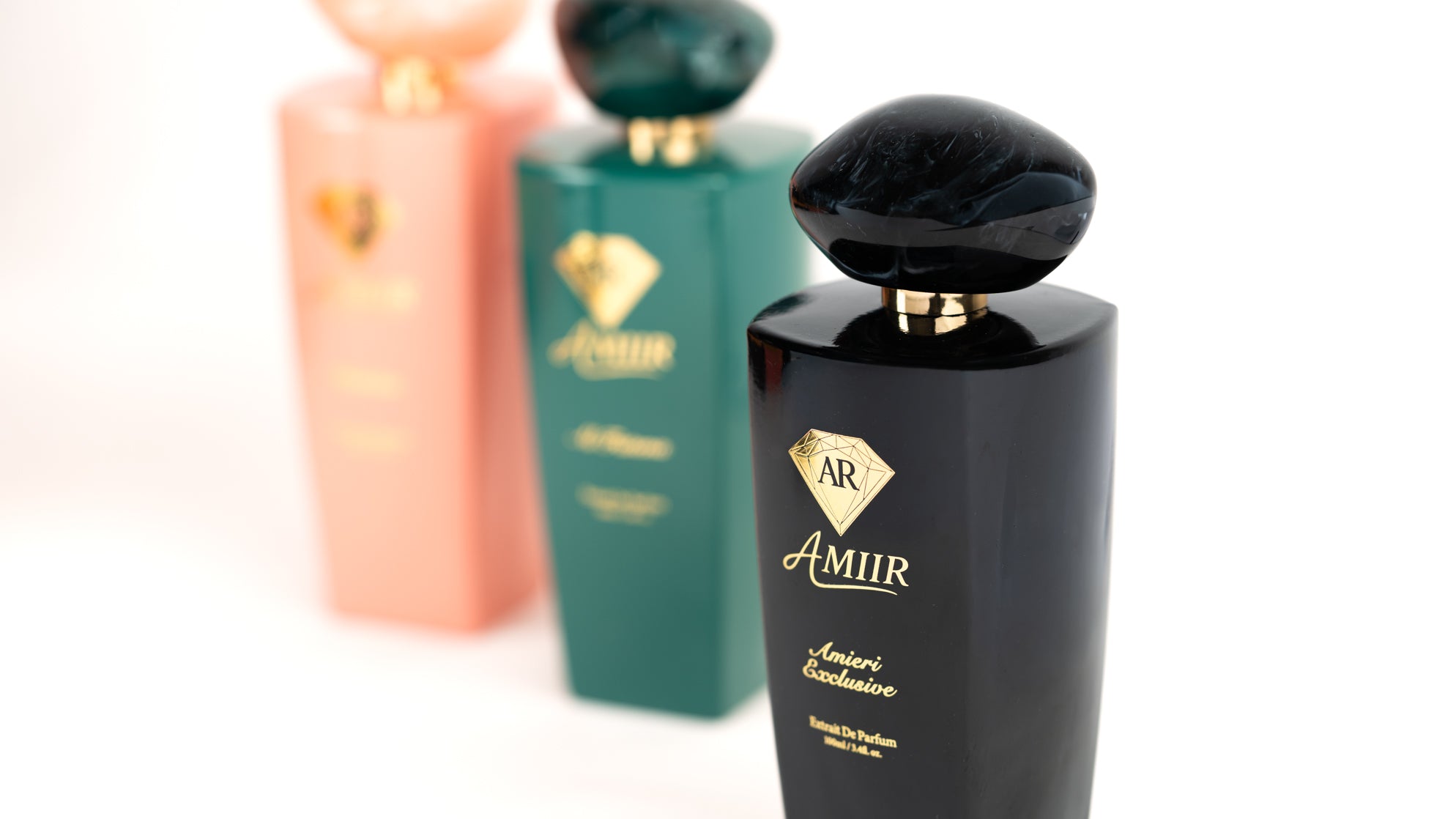Amiir Scents Amieri Exclusive extrait de parfum bottle in black, with blurred perfume collection on a white background