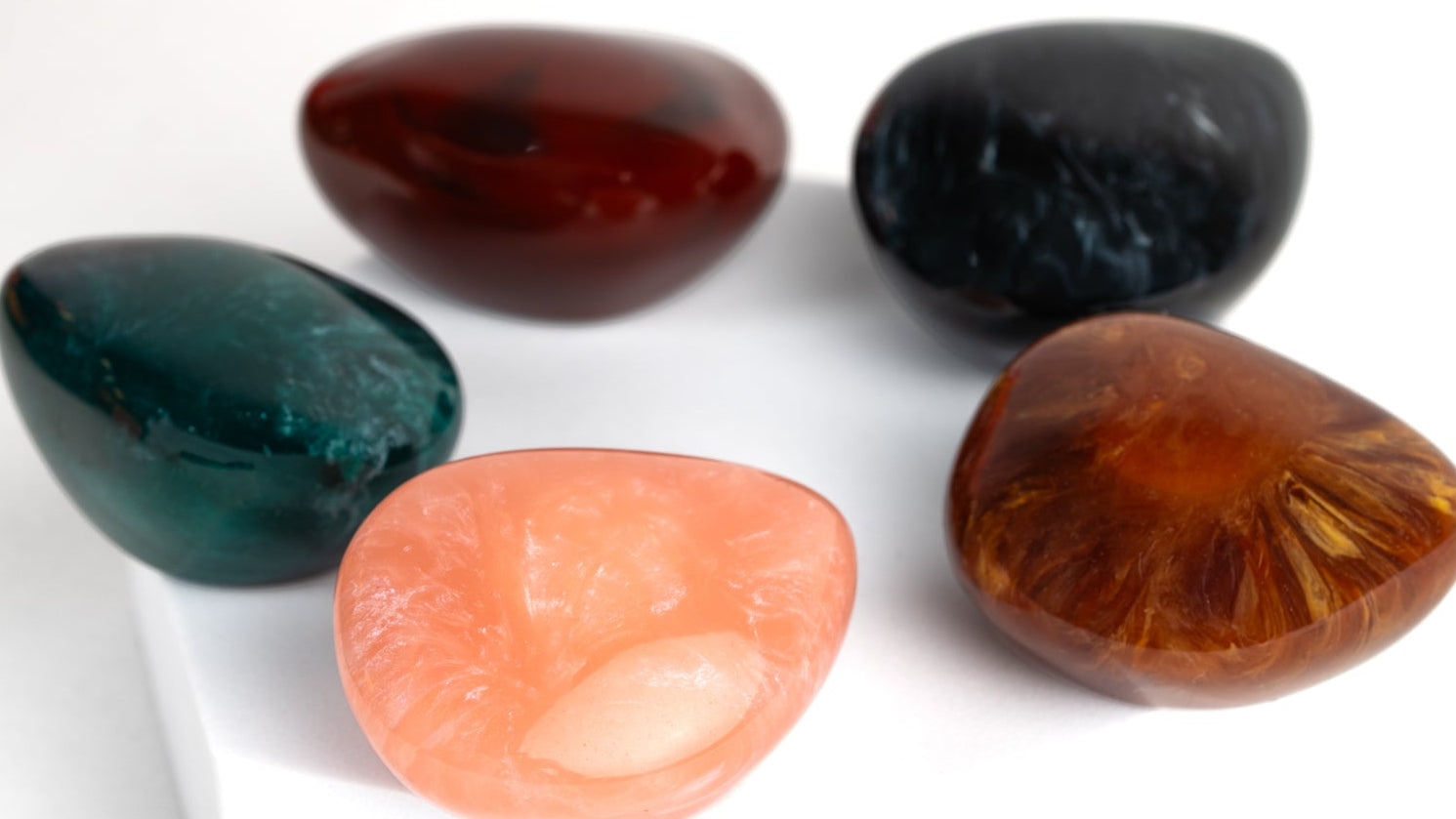 Five colorful stone-shaped perfume caps on a white background