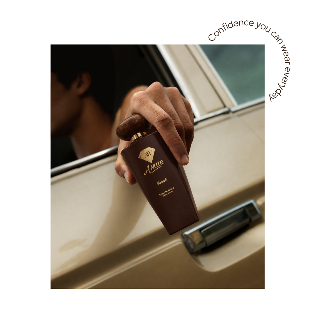 Luxury advertising image for AMIIR Gazab perfume. A hand holds the Gazab brown bottle outside the window of a classic cream-colored car. The perfume is shown in the foreground with a rounded marble-effect cap, gold neck, and gold label details. In the background, a blurred man sits inside the car, creating an elegant, warm, and sophisticated atmosphere. The scene conveys exclusivity, premium lifestyle, and a high-end masculine fragrance.